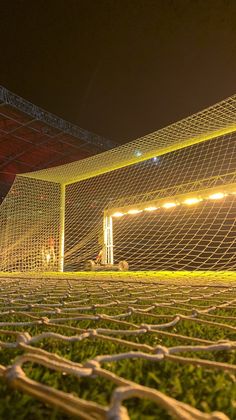 a soccer goal with the lights on and grass growing in front of it at night