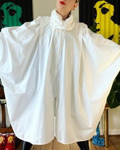 "WINGS. Incredible Vintage 1980's bright white cotton blend batwing jacket with stunning convertible gathered collar and a wingspan to float along your day in. The total package for seasonal layering. Fits a range of sizes (I'm about a M) Up to 40\" bust (on the half) 41\" length Unlined 47/27/26 poly/cotton/nylon Center front zipper closure Gathered convertible high neck Pleated shoulder with gathering Light shoulder pads (can be removed) Curved hem Batwing sleeve with single cuff button closur Oversized White Cape Outerwear, White Long Sleeve Cape For Spring, White Long Sleeve Spring Cape, Fashion Design Sketchbook, Girls Jacket, Batwing Sleeve, Bat Wings, High Collar, Eminem