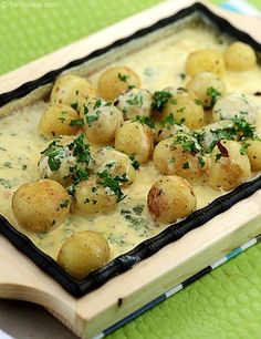 a wooden tray topped with potatoes covered in cheese and parsley on top of a green tablecloth