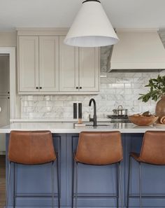 a kitchen with white cabinets and brown leather chairs in front of an island countertop