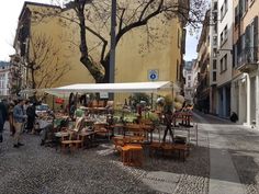 an outdoor market with tables, chairs and umbrellas in the middle of a cobblestone street