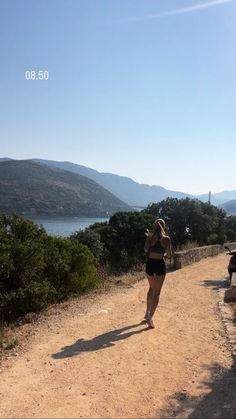 a woman walking down a dirt road next to a lake