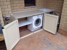 an open cabinet with a washer and dryer in it on the ground next to a brick wall