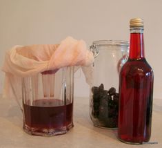 two bottles with liquid in them sitting next to each other on a counter top, one filled with blackberries and the other empty