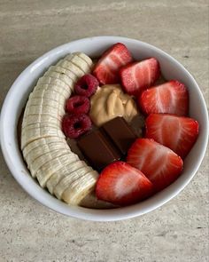 a white bowl filled with sliced bananas, strawberries and chocolate