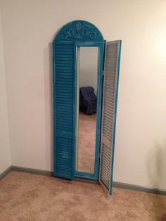 a room with a mirror and blue shutters on the door, in front of a white wall