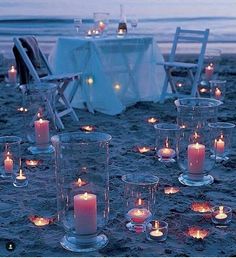 many lit candles are placed on the sand near chairs and tables with white linens