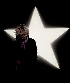 a man standing in front of a star with dreadlocks and a purple tie