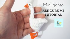 a hand holding a tiny crocheted white bird with an orange beak and tail