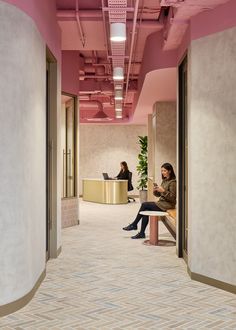 two people sitting on a bench in the middle of an office building with pink walls