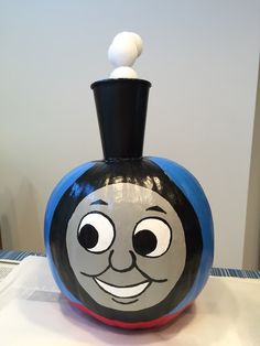 a black and blue vase with a face painted on it's side, sitting on a table