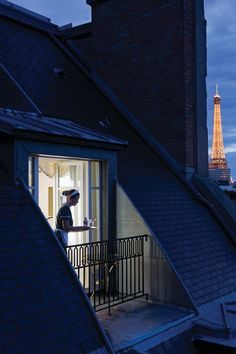 a woman standing on a balcony in front of the eiffel tower at night