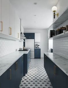 a long narrow kitchen with blue cabinets and white counter tops, along with black and white tile flooring