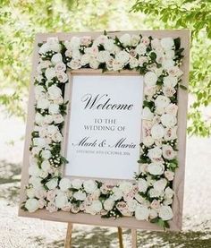 a welcome sign with white flowers on it and greenery around the frame is shown