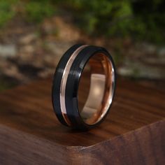 a wedding band with black and rose gold inlays sits on a wooden surface