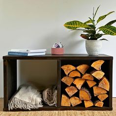 a wooden shelf filled with logs next to a potted plant on top of a rug