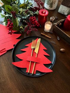 a black plate topped with red paper cut out christmas trees next to candles and greenery