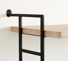 a wooden shelf with black metal brackets and a white wall in the backround