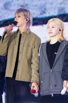 two people standing next to each other on stage with microphones in their hands and one person wearing headphones