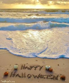 happy halloween written in sand on the beach with ocean waves and sun shining through clouds