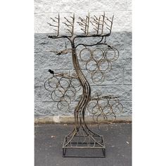 a metal tree with many circles and birds on it's branches in front of a gray brick wall