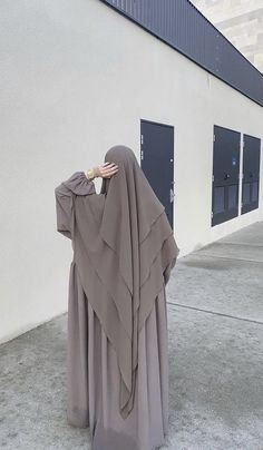 a woman in a long dress is covering her face with her hands and standing outside