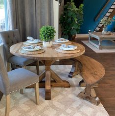 a dining room table with two chairs and a bench in front of the window, next to a potted plant