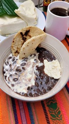 there is a bowl of food on the table next to a cup of coffee and two slices of pita bread