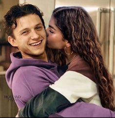 a young man and woman are hugging in the kitchen, one is wearing a purple hoodie