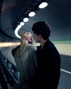 two people standing next to each other in a subway station, one kissing the other