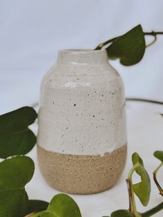 a white vase sitting on top of a table next to some green leafy branches