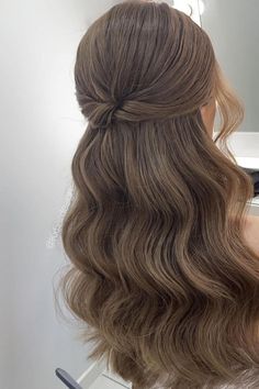 the back of a woman's head with long wavy hair in front of a mirror