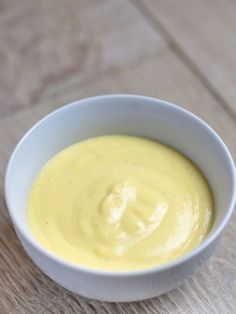 a white bowl filled with yellow sauce on top of a wooden table