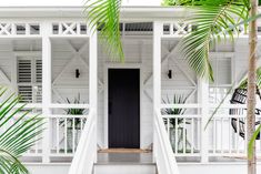 a white house with palm trees and stairs leading up to the front door that has a black door