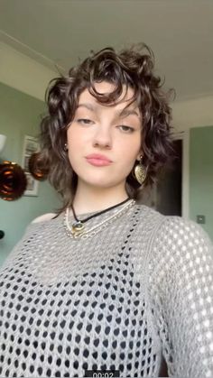 a woman with short curly hair wearing a sweater and statement earrings is looking at the camera