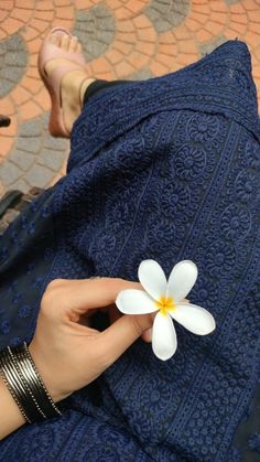 a woman is holding a white flower in her lap while sitting on the floor with her legs crossed