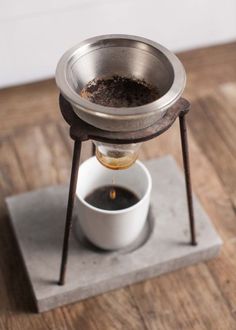 an espresso machine with coffee in it on a wooden table next to a white cup