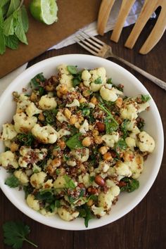 a white bowl filled with cauliflower, nuts and parsley on top of a wooden table