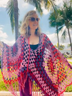 a woman standing in the grass wearing a red and blue crocheted shawl