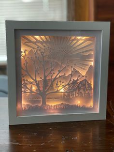 a paper cut art with a tree and house in the background on a wooden table