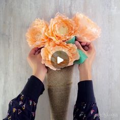 two hands holding up an orange flower in front of a white wooden wall with text overlay that reads, how to make paper flowers