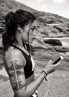 a woman with tattoos on her arm and headphones is looking at her cell phone