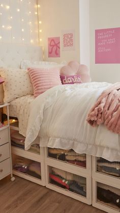 a white bed with pink pillows and blankets in a bedroom next to a night stand