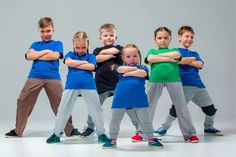 five children in blue shirts and grey pants posing for the camera with their arms crossed