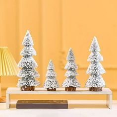 there are three small christmas trees on the table next to each other and a lamp in the background