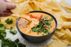 a person dipping tortilla chips into a bowl with salsa and cilantro