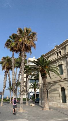 a person is walking down the street in front of some palm trees and a building