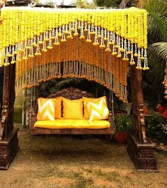 a bed covered in yellow and white pillows next to a lush green forest filled with flowers