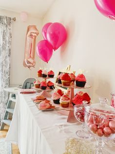 a table topped with lots of cupcakes and balloons