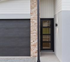 the front door to a house with a brick wall and black garage door on one side